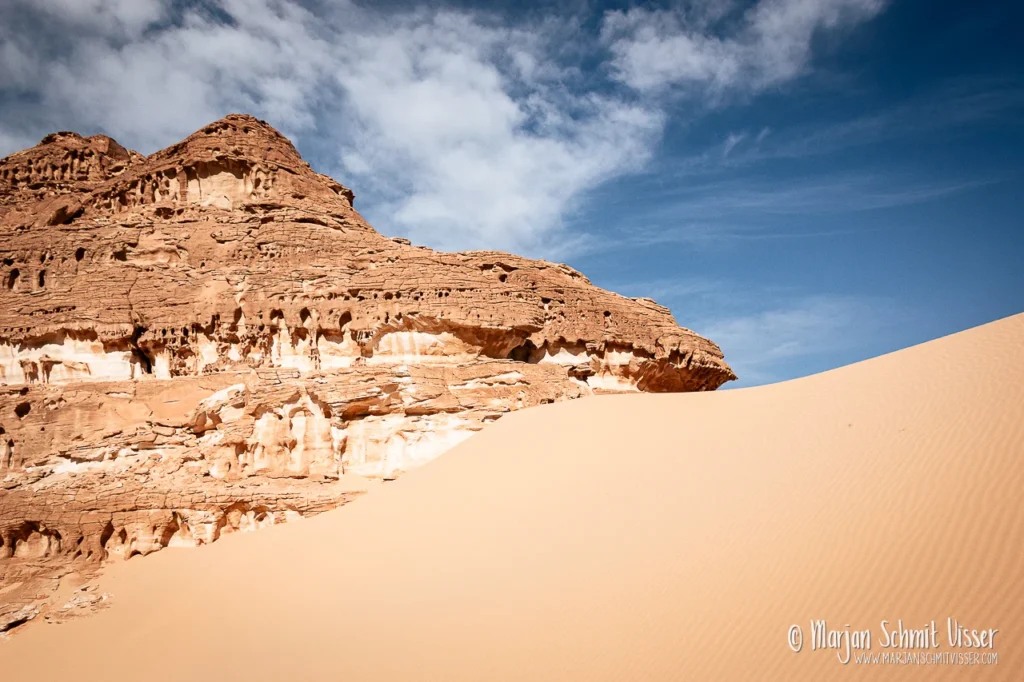 Rotsformatie en zandduin in de Sinaïwoestijn, Egypte, onder een blauwe lucht met lichte bewolking.