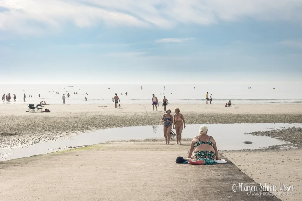 Reisfotografie 10 Reisfotografie Groepen strandbezoekers wandelen en ontspannen aan de kust bij zacht licht, met ondiepe waterplassen en een heldere lucht op de achtergrond.